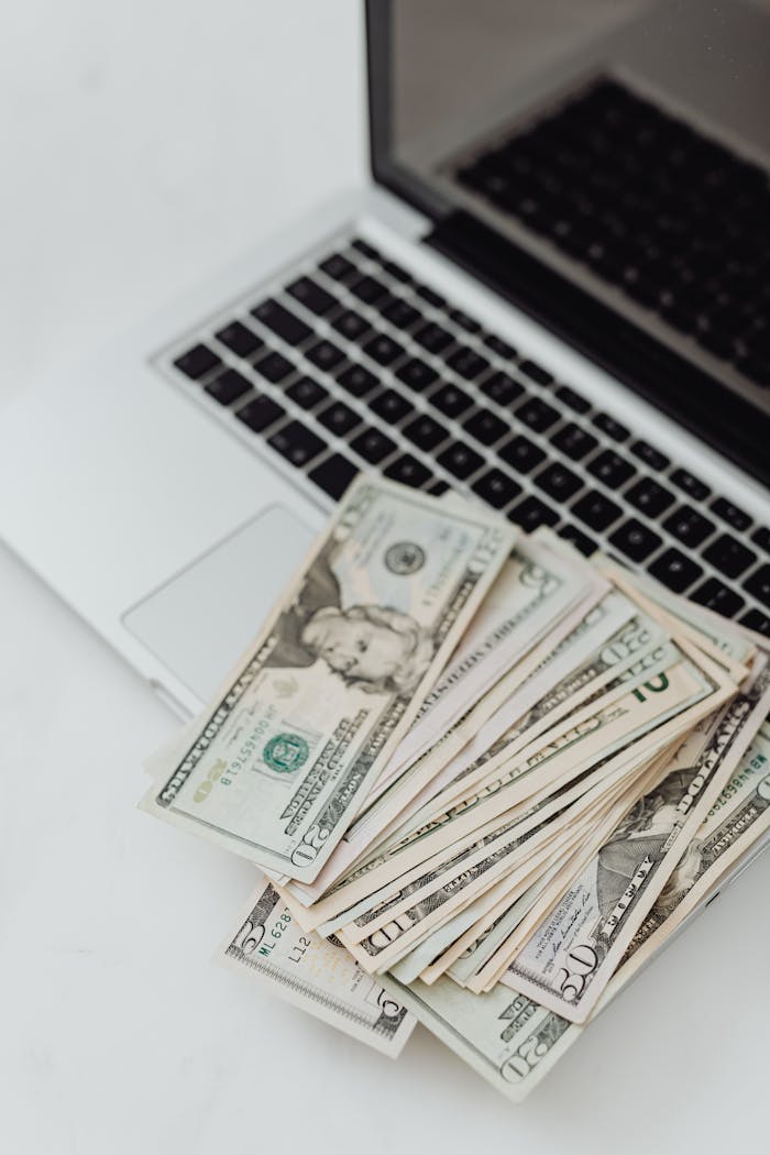 Stack of US dollar bills on a laptop keyboard representing online finance and budgeting.